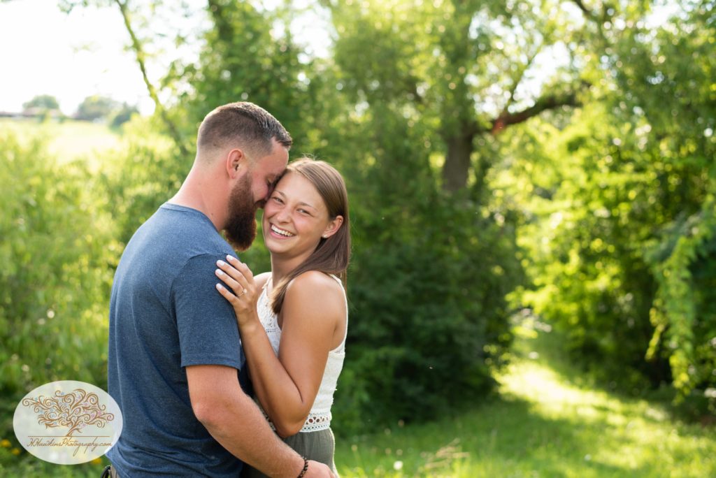 Bride to me smiles at camera during engagement session as groom nuzzles in to her 