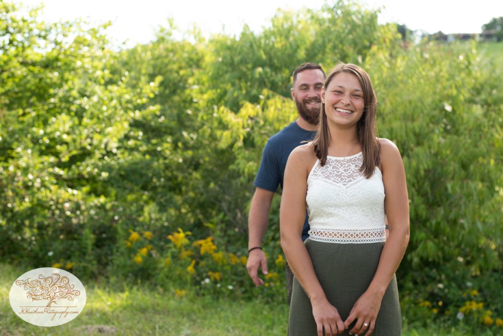 Groom sneaks up behind bride as she smiles at the camera