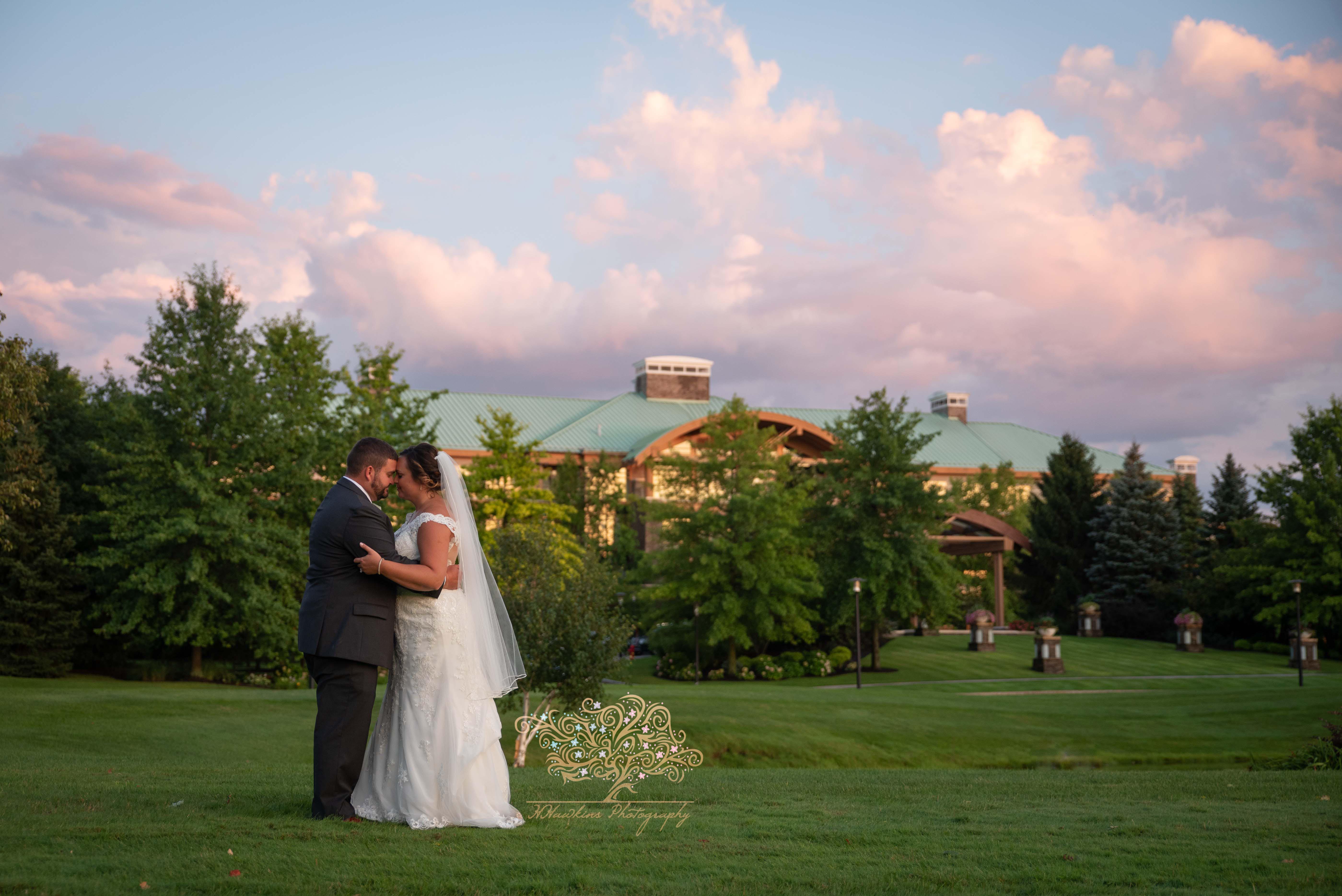 Bride and groom on lawn of Turning Stone's Lodge with colored sunset clouds in the sky