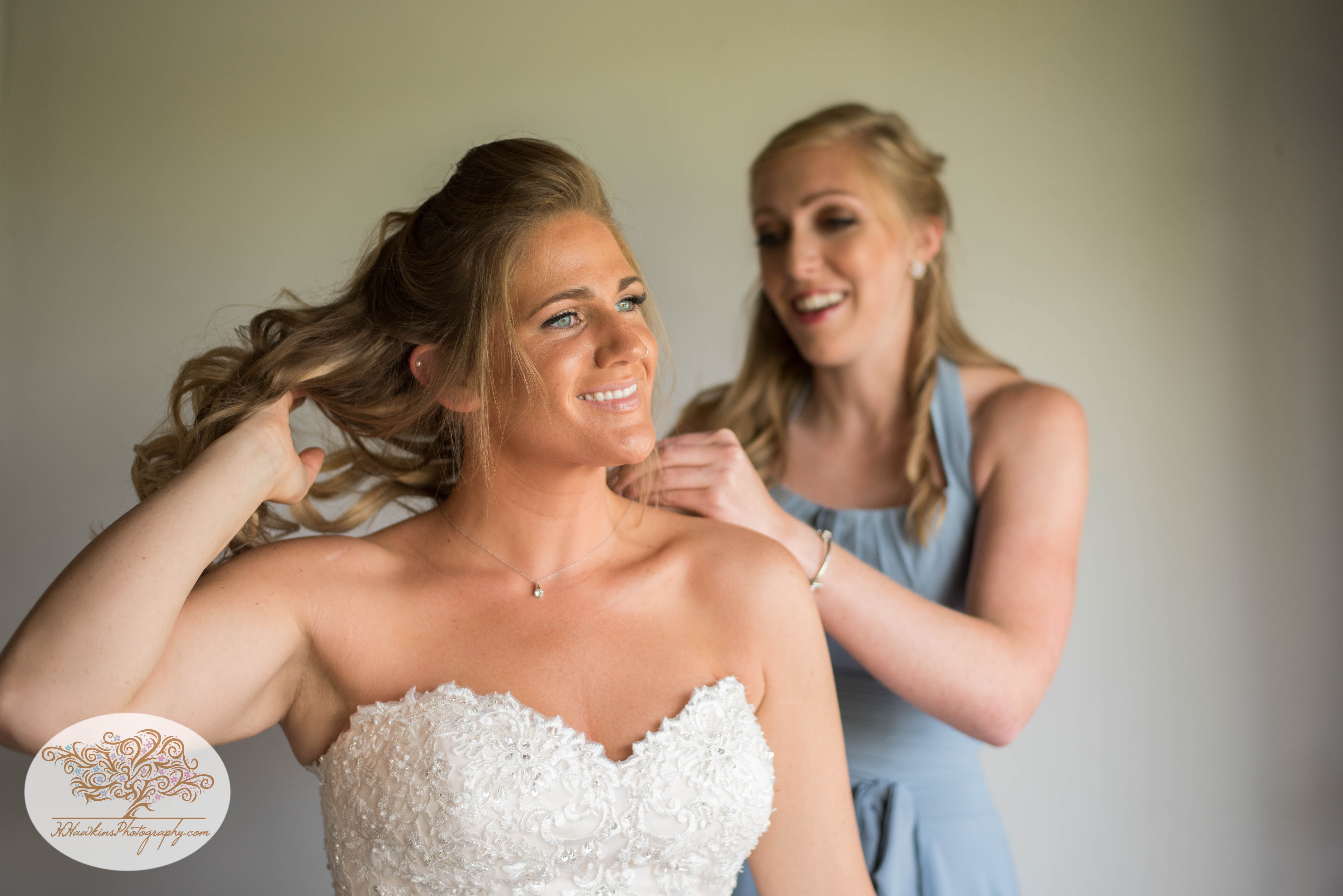 Bride is helped by bridesmaid to put on her necklace for barn wedding upstate NY