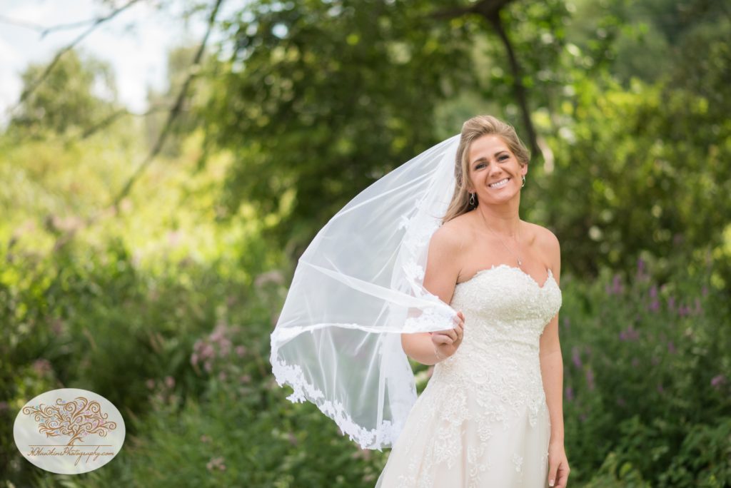 Bride holds her veil as breeze blows during her Upstate NY barn wedding