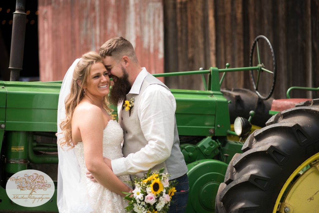 Bride and groom laugh at each other in front of John Deere tractor during Upstate NY barn wedding by Syracuse photographer