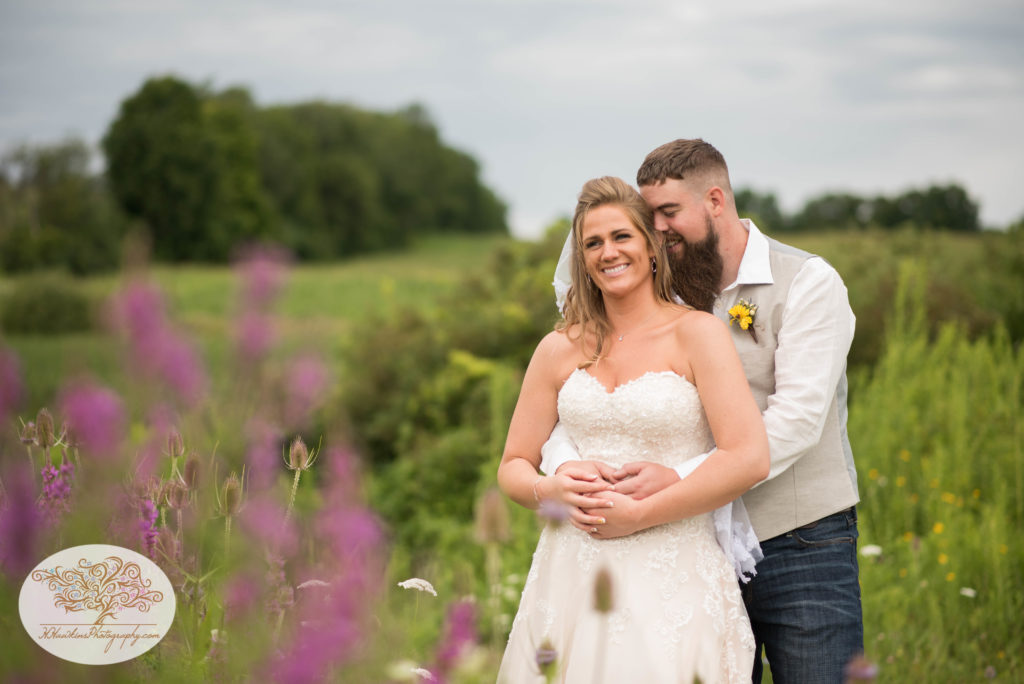 Bride and groom pose as he makes her laugh in a field of purple wildflowers