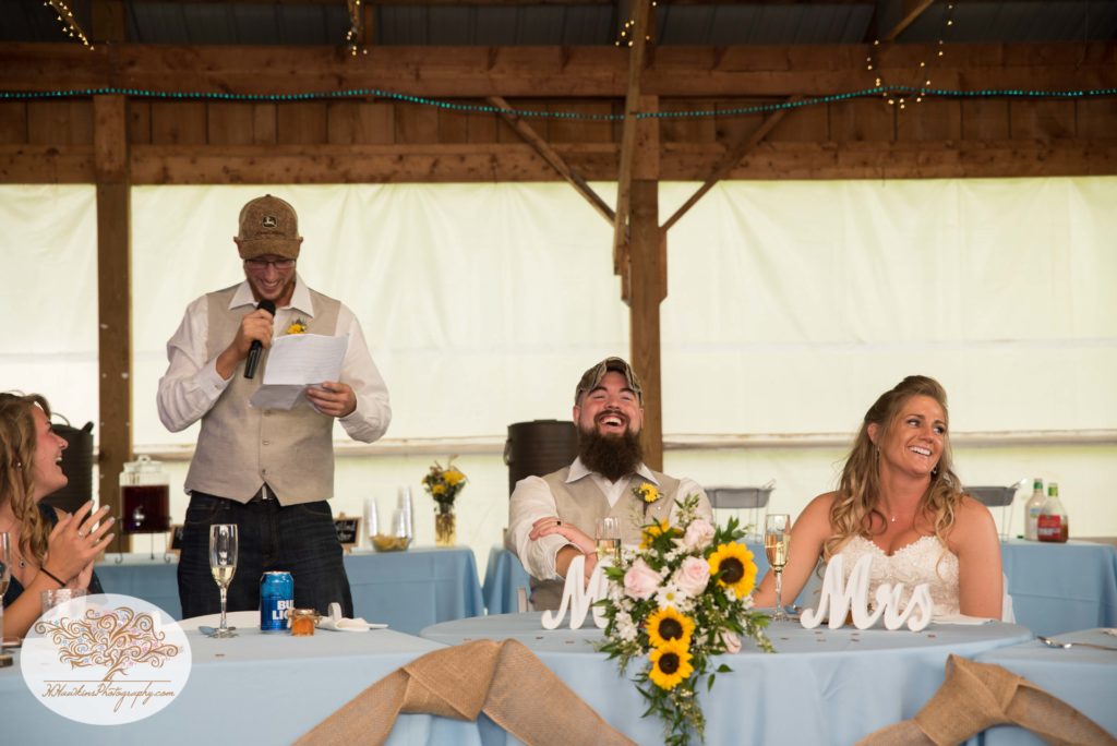 Best man gives speech while bride and groom laugh during Upstate NY barn wedding reception