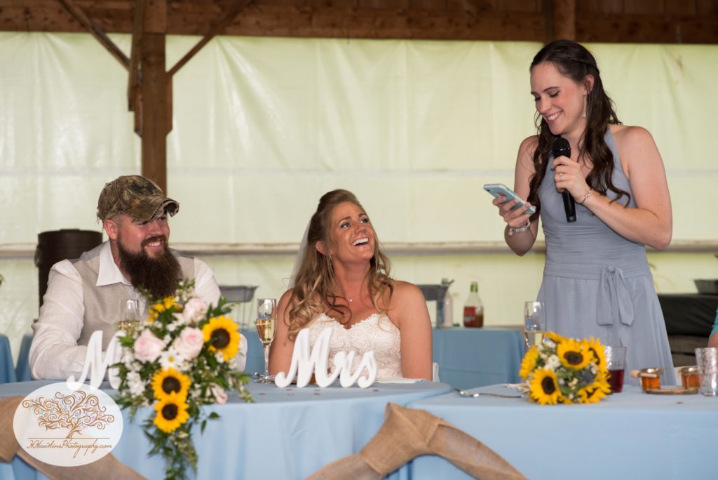 Maid of honor gives speech while bride and groom laugh during Upstate NY barn wedding reception