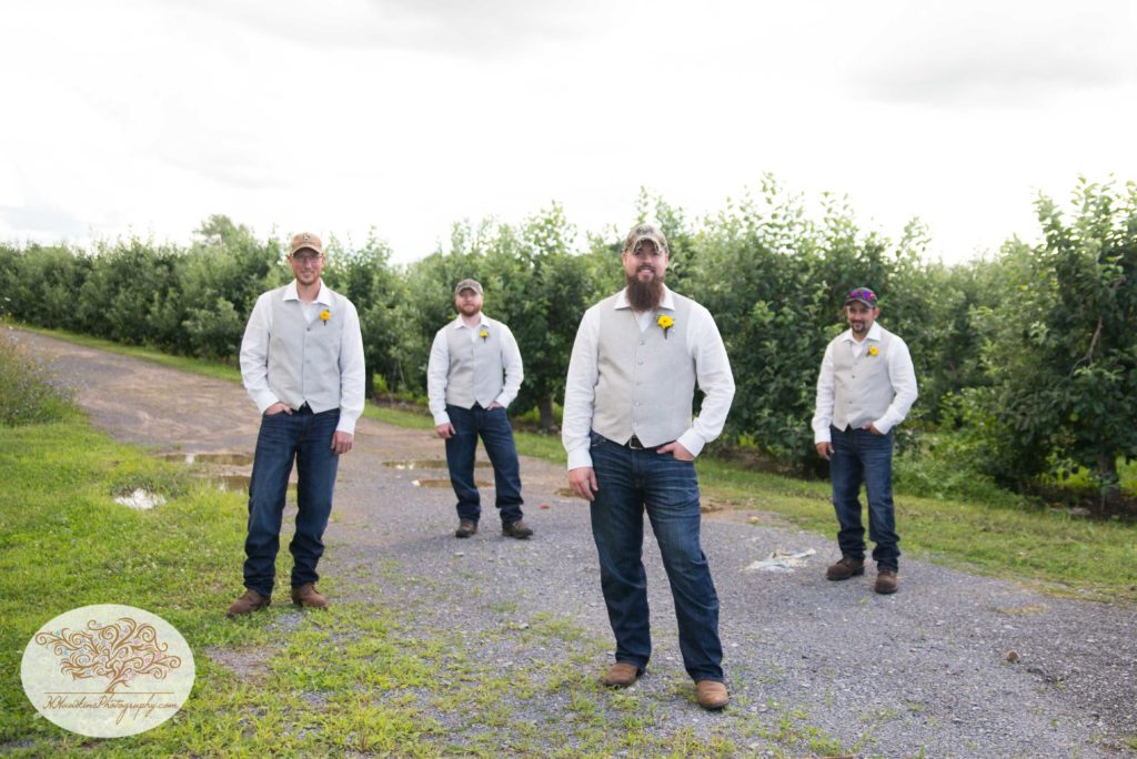 Groomsmen in cowboy boots and hats stand casually in apple orchard