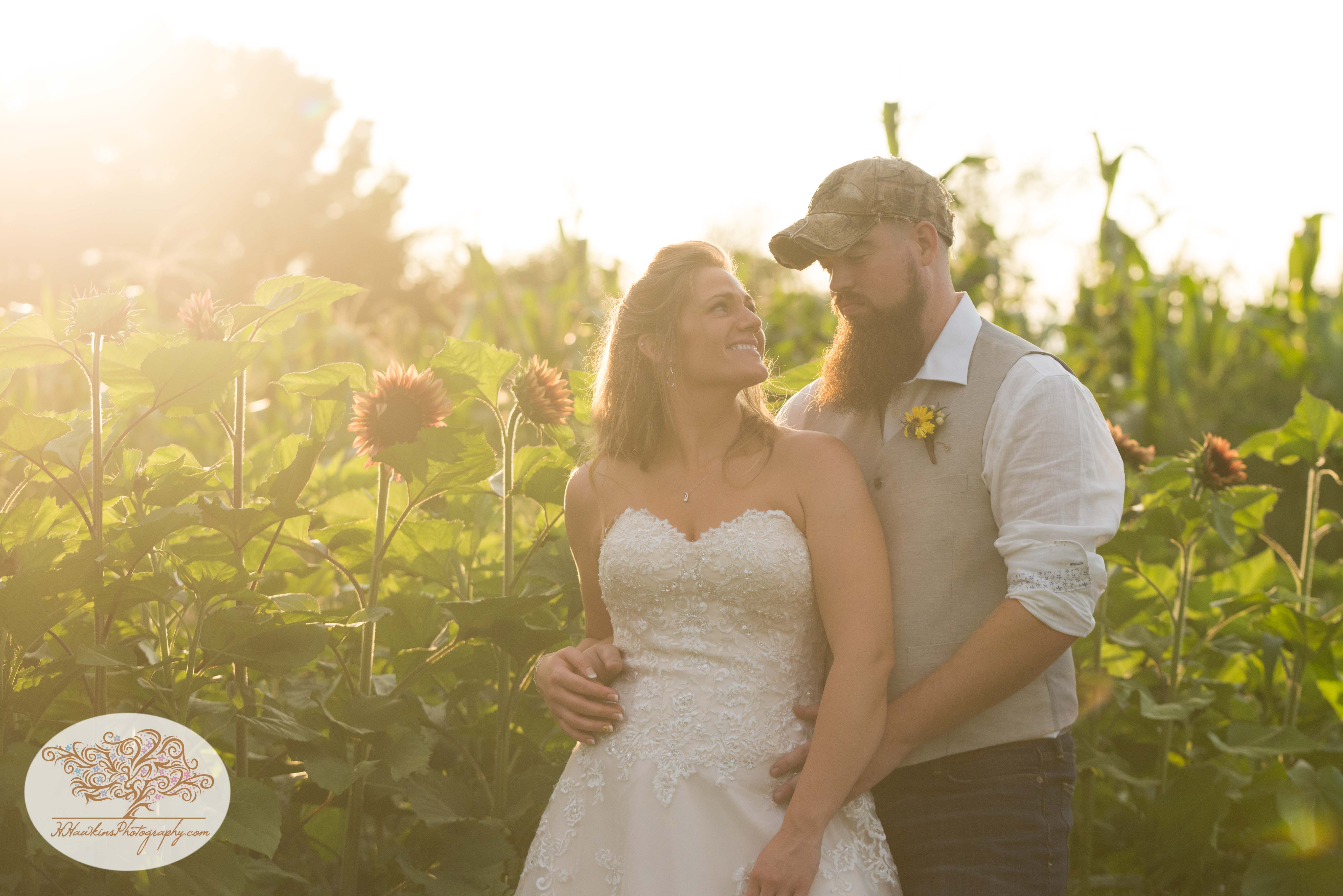 Bride and groom stand in a field of sunflowers during golden hour by Syracuse wedding photographer