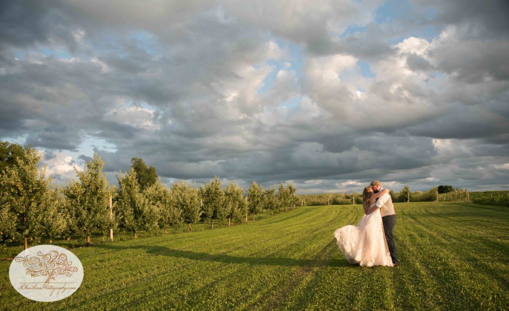 Bride pops her leg and kisses the groom in a field at Owen Orchard