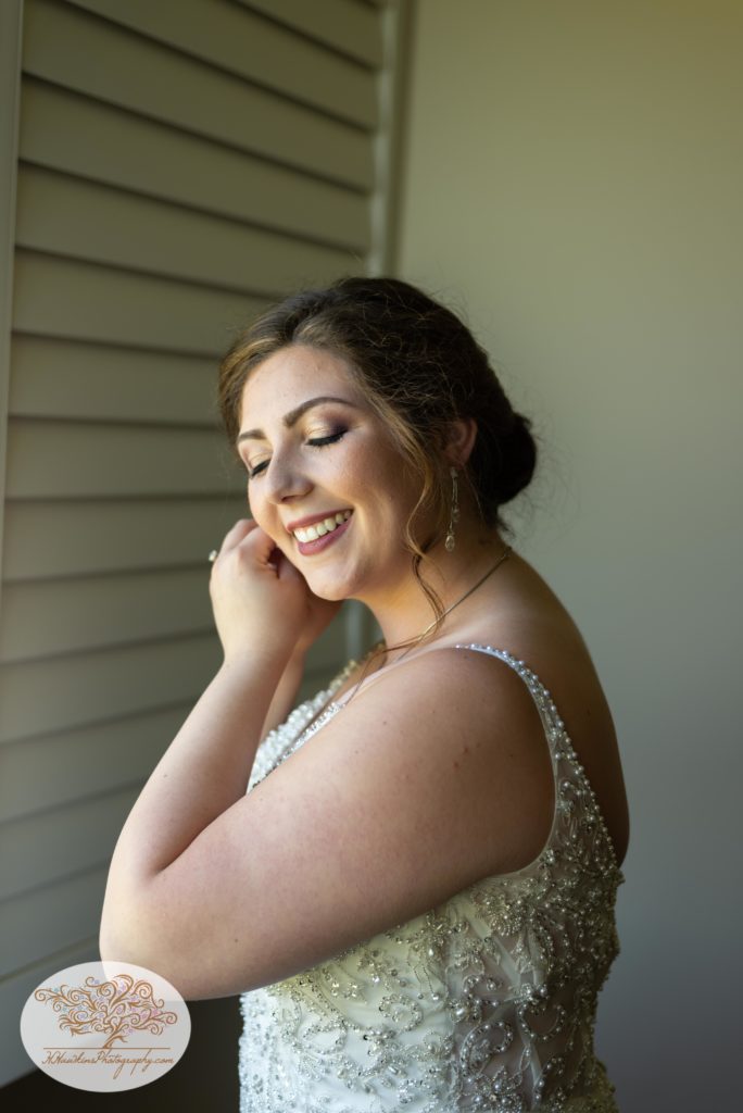 Bride puts her earring on as she stand in her wedding dress