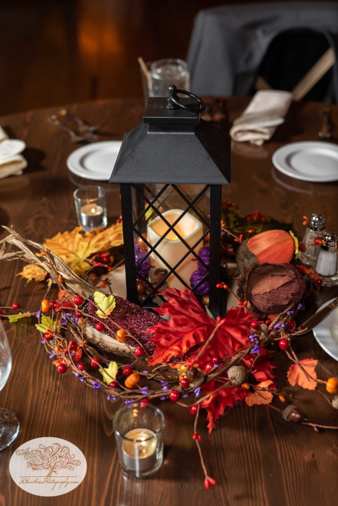 Wedding centerpiece with fall decor made up of a lantern, autumn leaves and candles