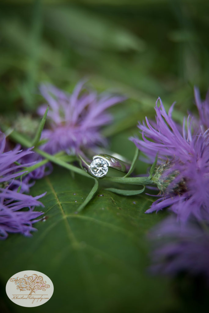 Diamond Engagement ring laying on a green leaf surrounded by purple flowers