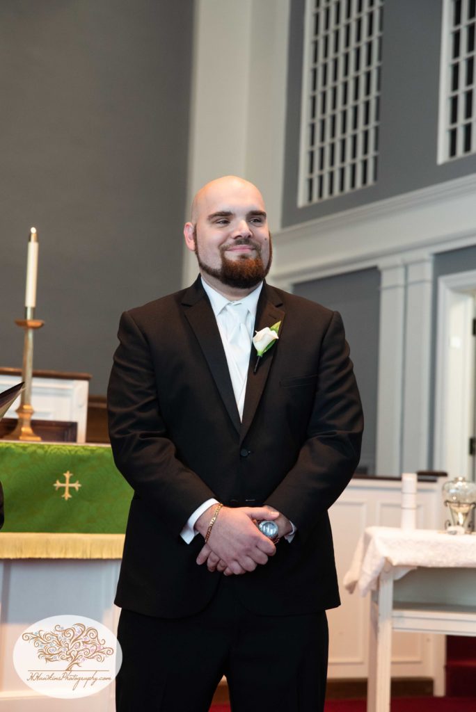 Groom smiling as he stands at the front of the church and see his bride for the first time