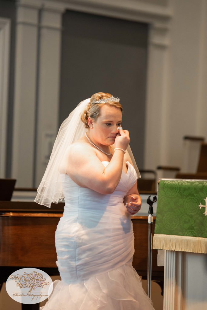 Bride wipes a tear away as she stands at the church altar on her wedding day