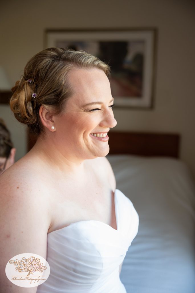 Bride smiling out the window as maid of honor laces up her wedding dress