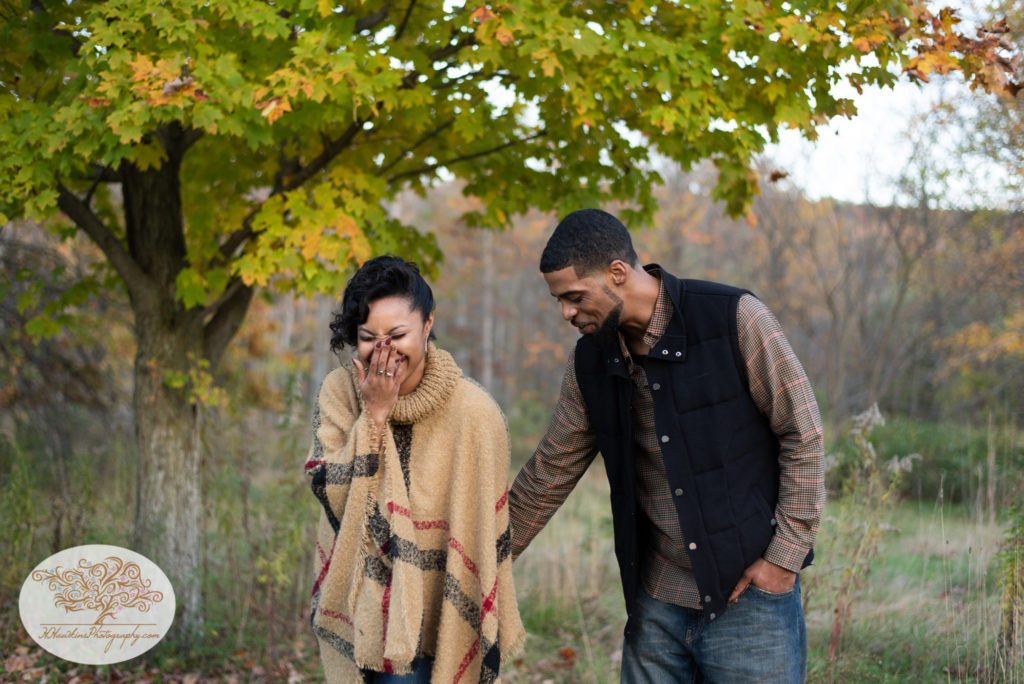 Bride to be covers her mouth as she giggles with her fiance during their autumn engagement pictures