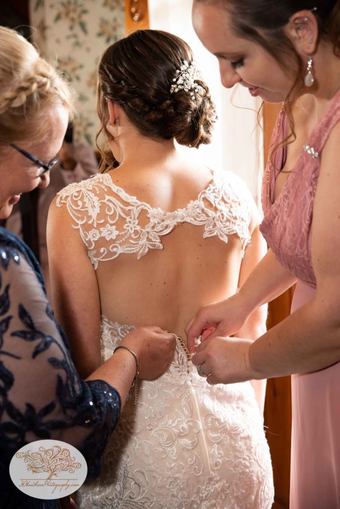 Bride getting her wedding dress buttoned up by Matron of Honor and mother