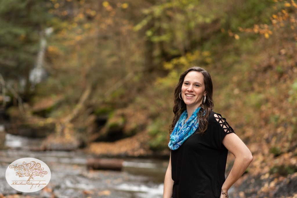 Bride looks at her groom who is off camera with fall background behind her