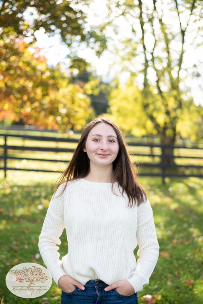 Girl smiles at camera for with the fall foliage behind her