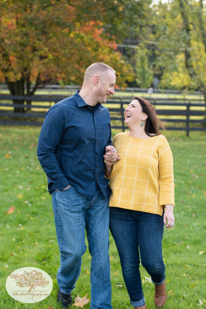 Husband and wife laugh together as they walk hand in hand during family portrait session