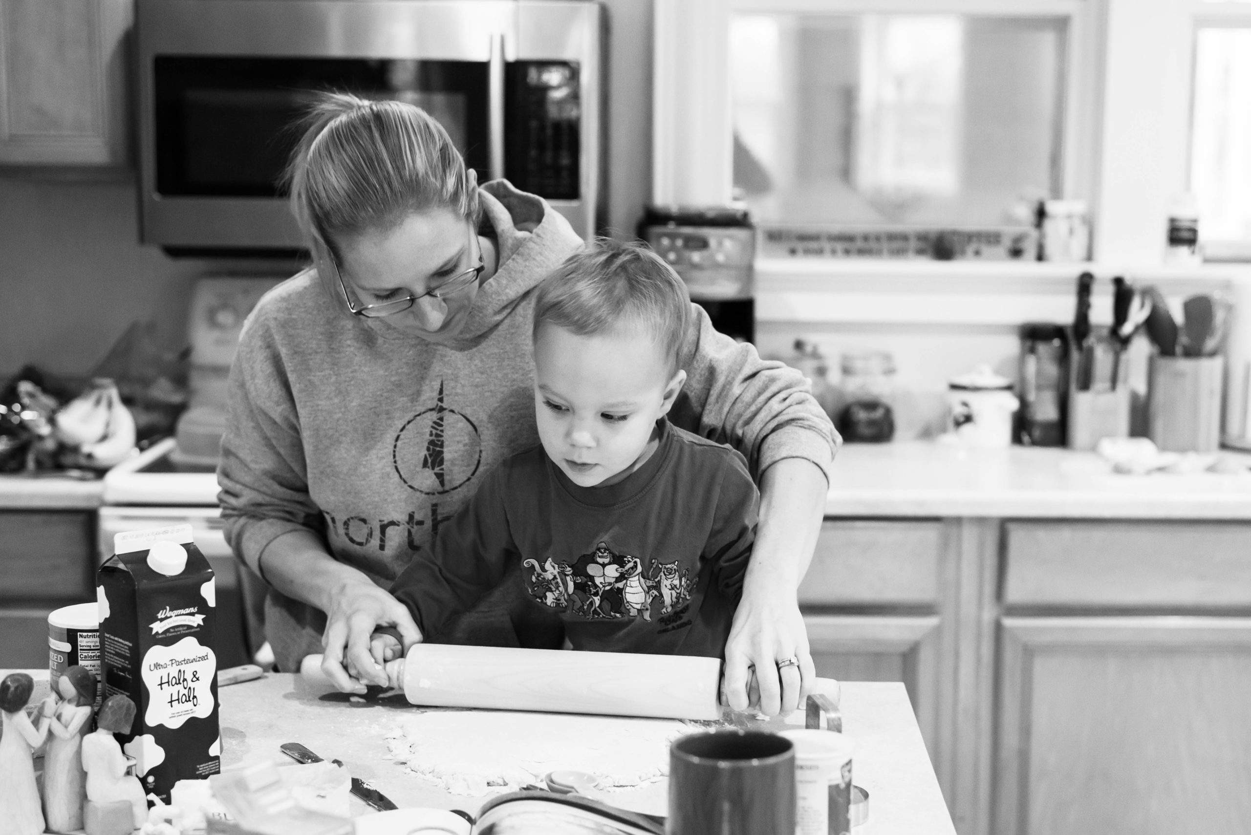 Mom and toddler roll out dough for breakfast on kitchen counter