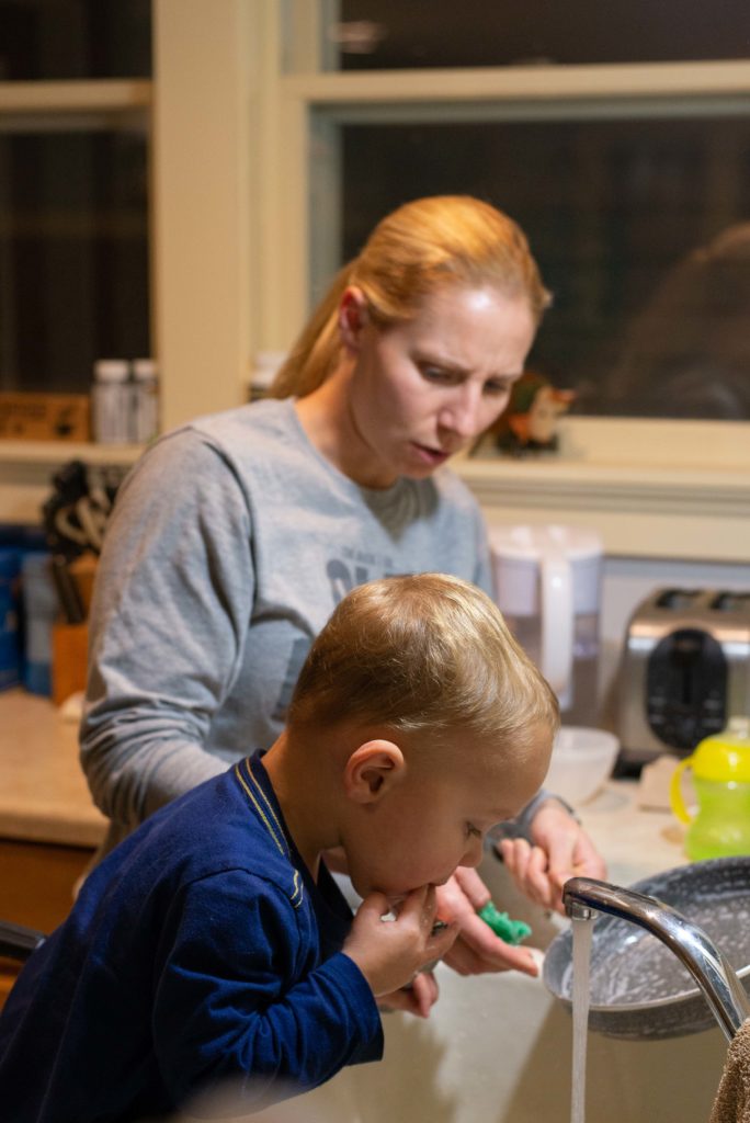 Mom scolds little boy for putting old food in his mouth while washing dishes