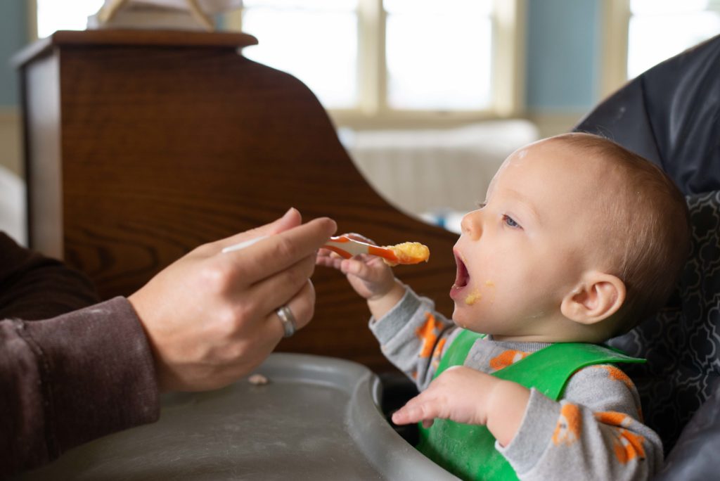 Baby opens his mouth to receive his food as dad spoons it into his mouth
