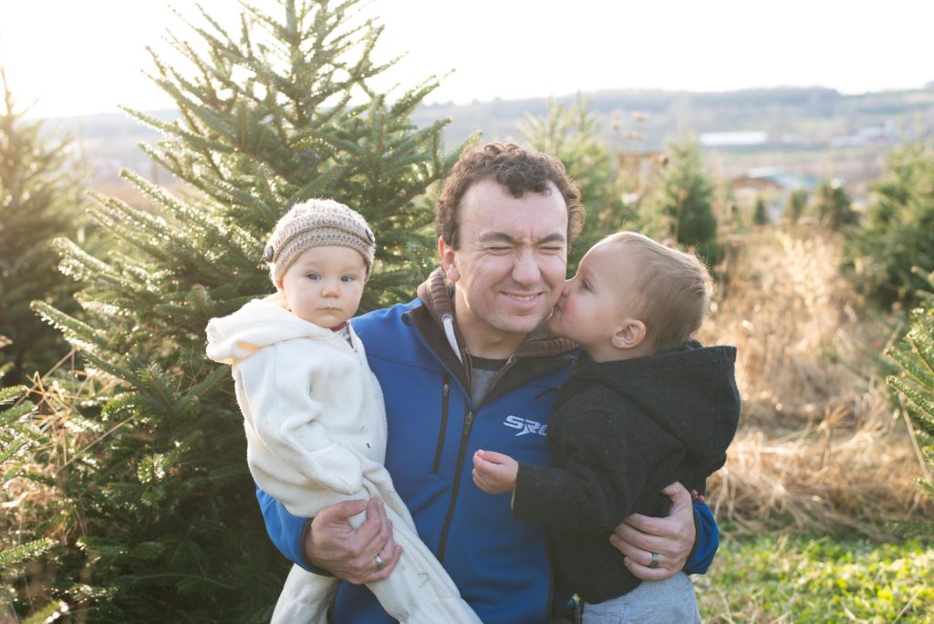 Toddler boy kisses daddy on the cheek at a christmas tree farm