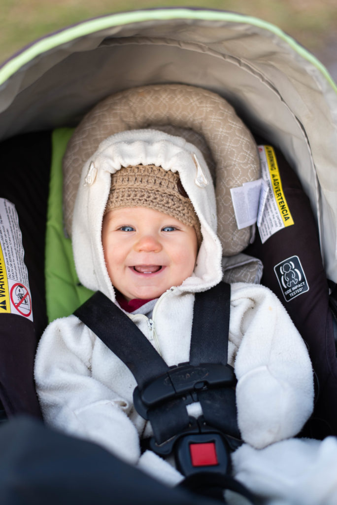 Baby strapped into his car seat smiles for his mom
