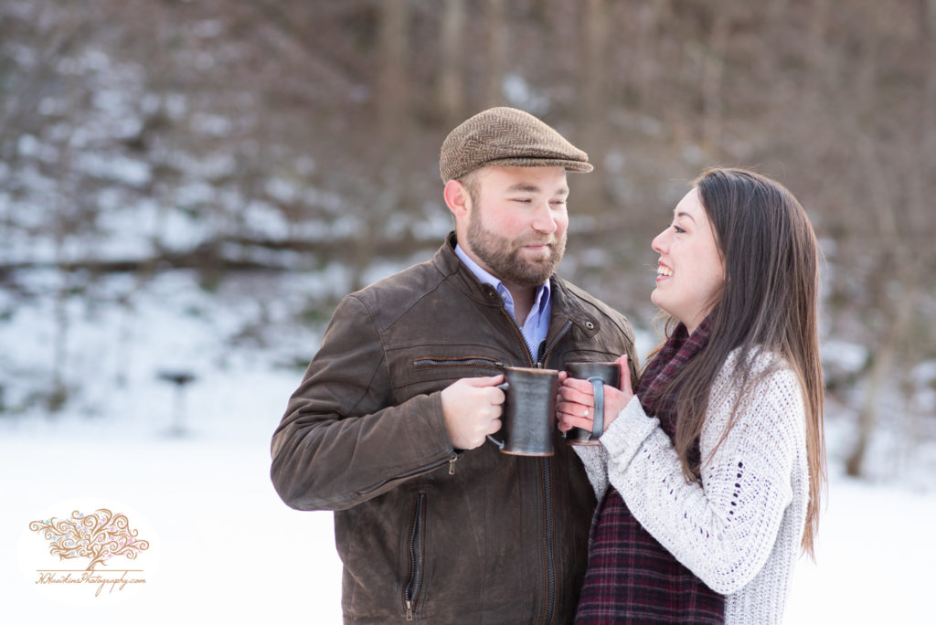 Bride and groom to be hold coffee mugs during their snowy engagement pictures