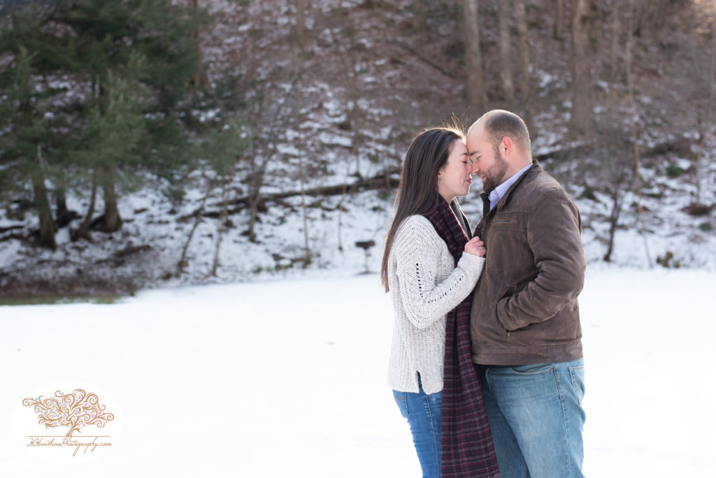 Bride and groom to be standing with their noses together during snowy engagement pictures session