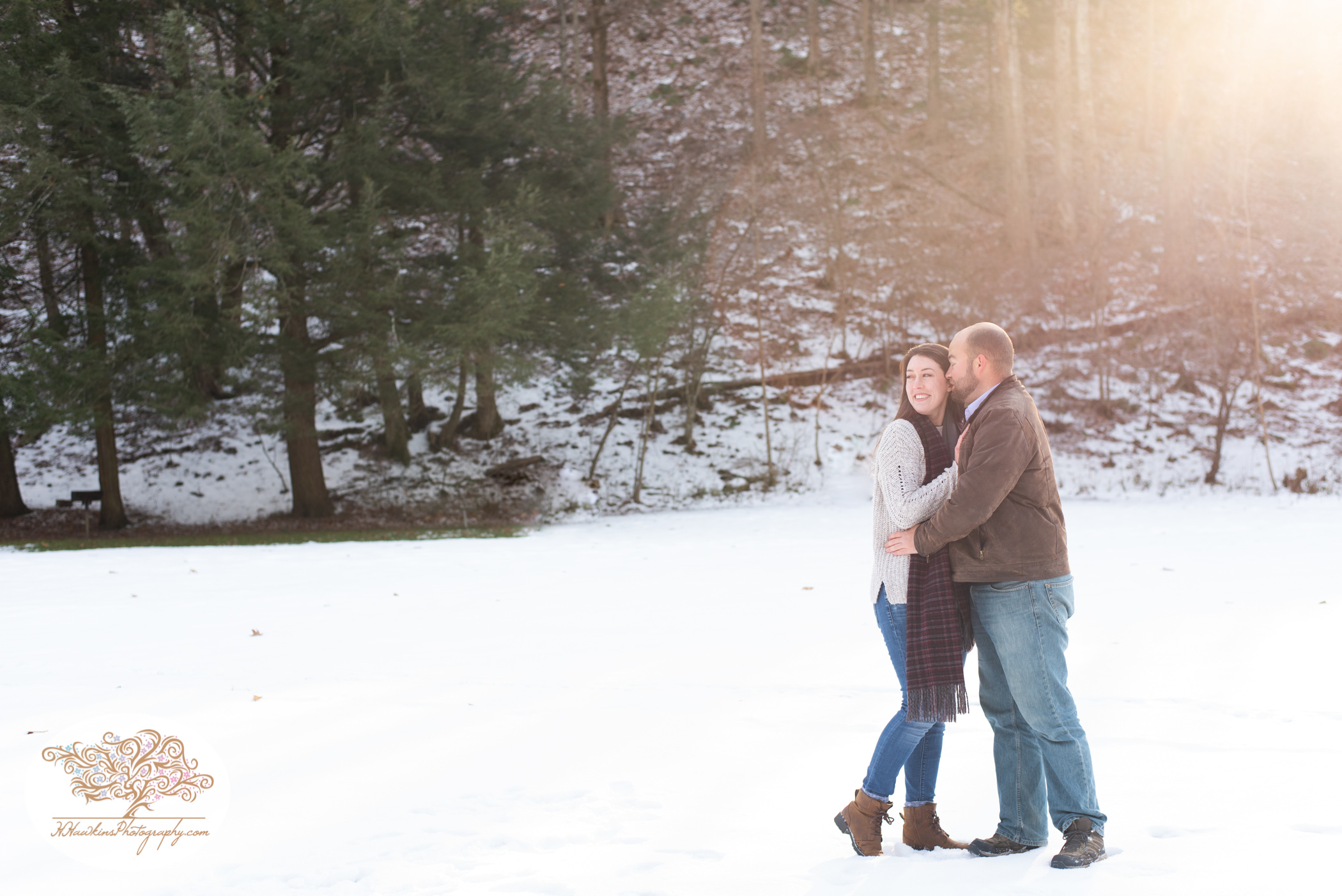 Epic snowy engagement picture of couple in the snow with sun peeking through the lens
