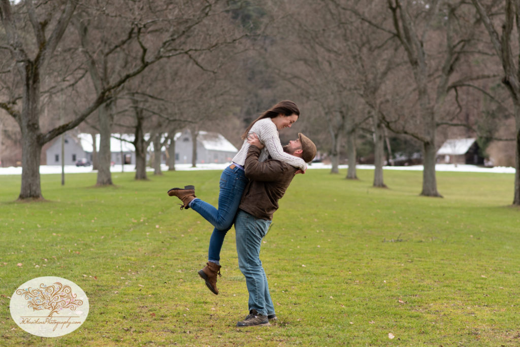 Groom to be lifts bride to be into the air while she pops her foot during their engagement session at Fillmore Glen