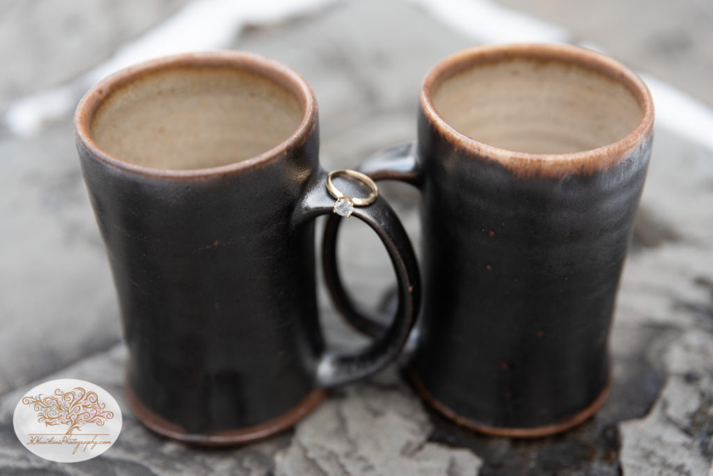 Diamond engagement ring balanced on two coffee mug hands