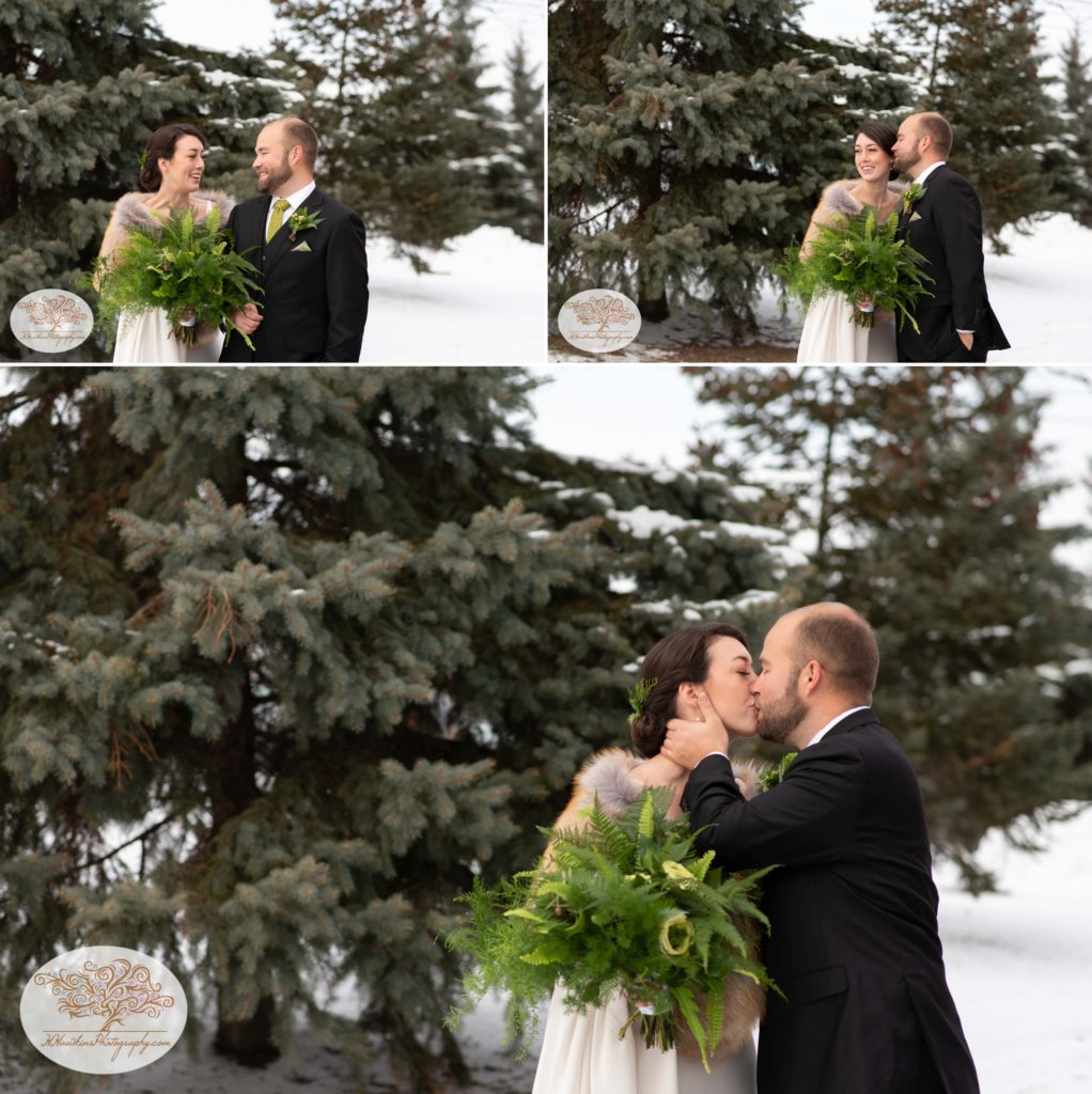 Bride and groom kiss and love each other in front of evergreen trees at Belhurst Castle