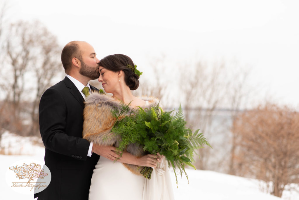 Groom kisses bride on the forehead during their portrait session on their wedding day