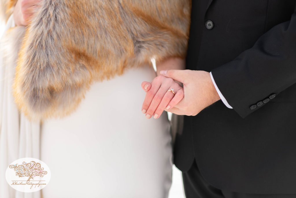 detail picture of bride and groom holding hands while she wears a white wedding dress and fur stole and he in his black suit