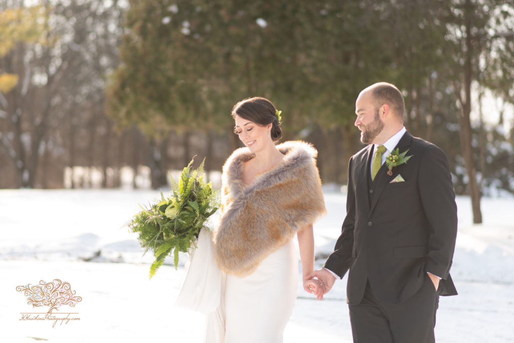 Bride and groom walking hand in hand through the snow with the sun at their back
