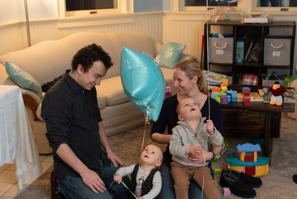 Mom, dad and two little boys play with birthday balloons for son's first birthday