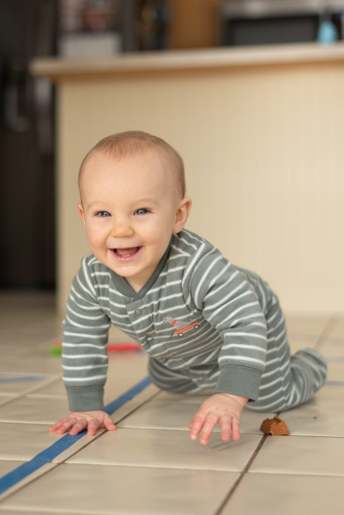 One year old crawling across floor towards camera smiling
