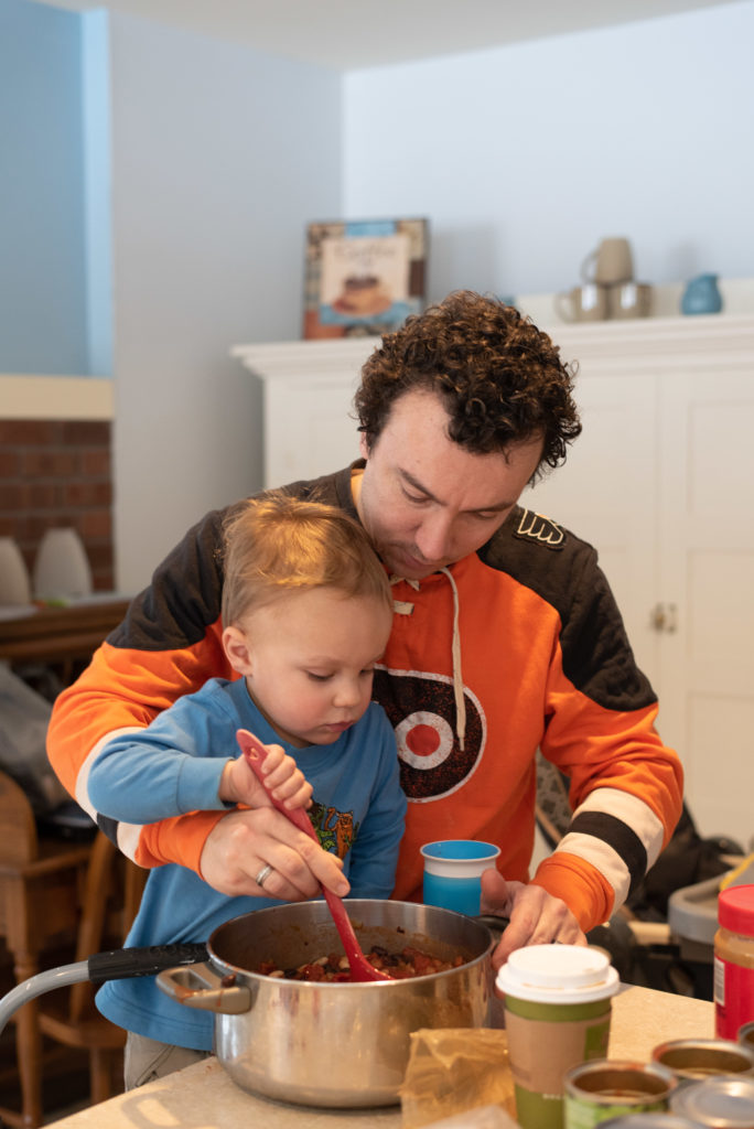 Dad helping little son make chili together at the kitchen counter