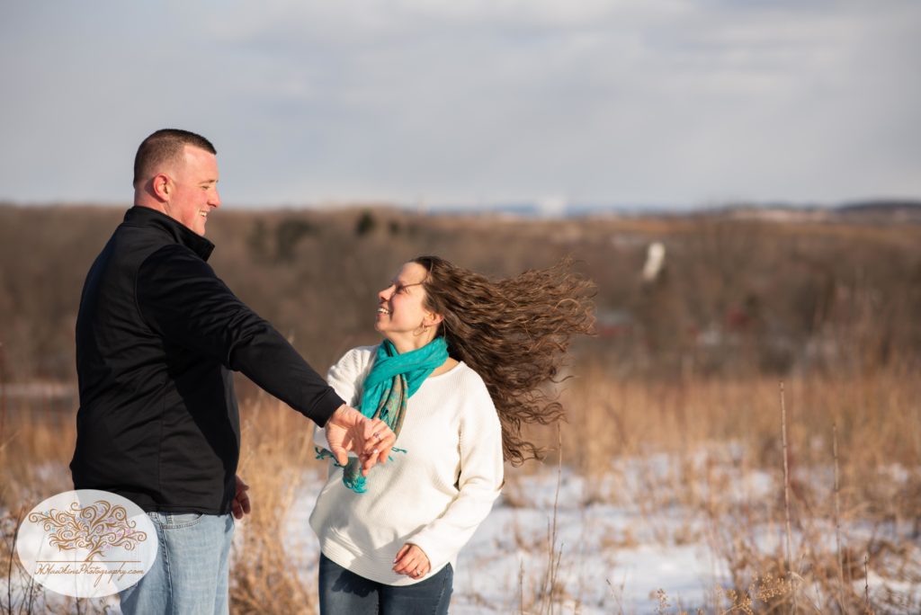 Groom to be spins bride to be during their engagement session in a snowy sunny field