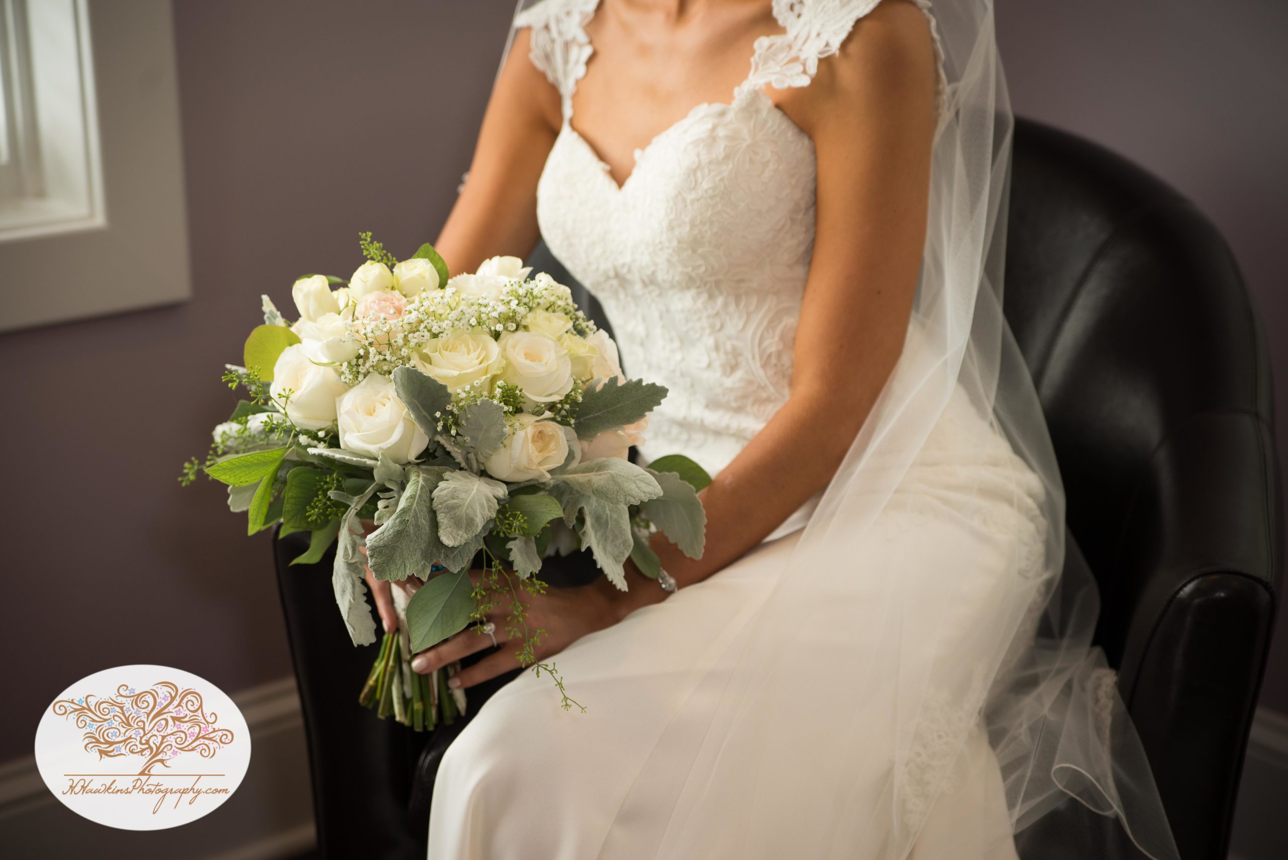 Bride sits in a chair in her lace wedding dress with a bouquet of white flowers in her lap