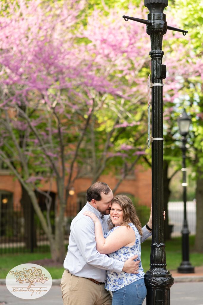 Bride and groom stand beside a black lamp post in front of a purple blossoming tree at Syracuse's Franklin Square Park
