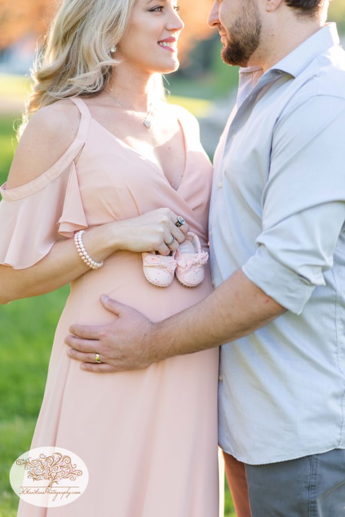 Mom and dad to be show off their little girl's baby shoes placing them on her pregnant belly