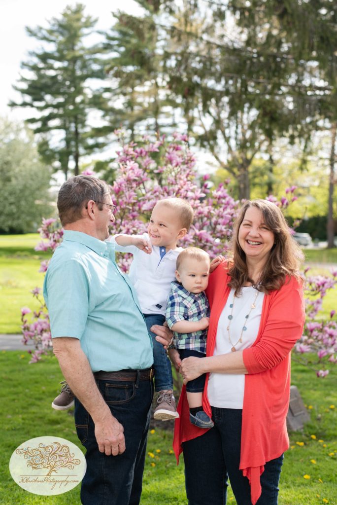 Grandparents and grandchild stand in front of pink magnolia tree at Hoopes Park in Auburn NY
