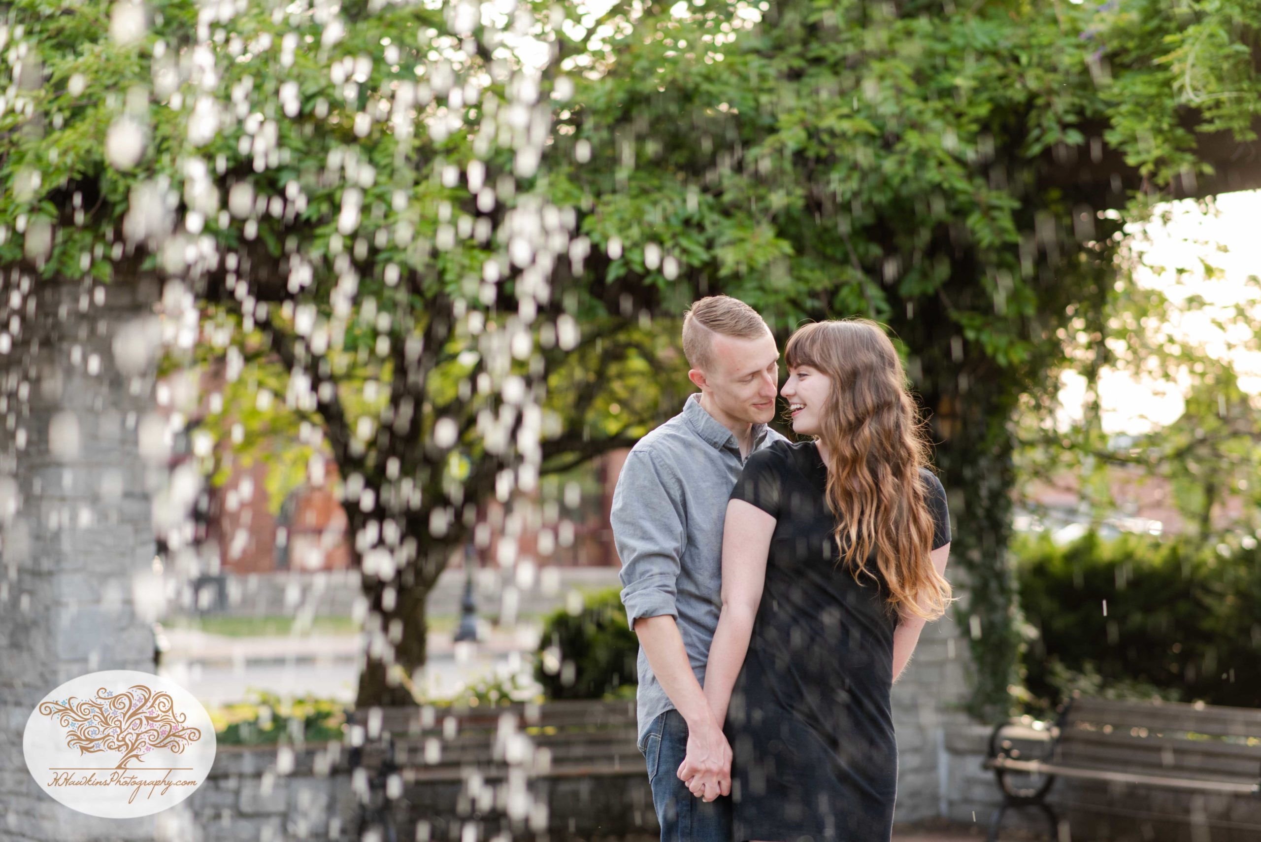 Bride and groom stand behind fountain at Franklin Square Park for their engagement pictures