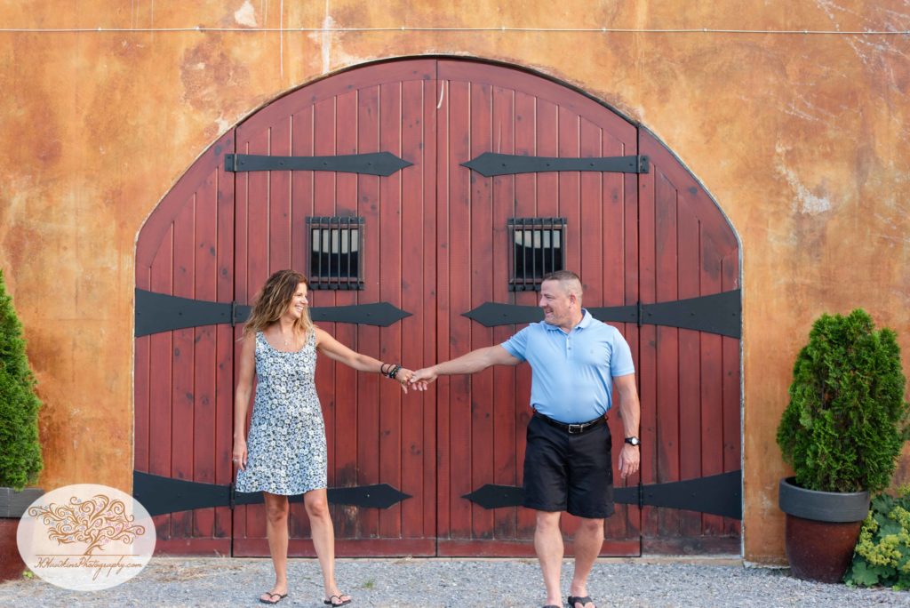 Bride and groom to be walk together in front of red Tuscan looking doors at Anyela's Vineyard in Skaneateles NY