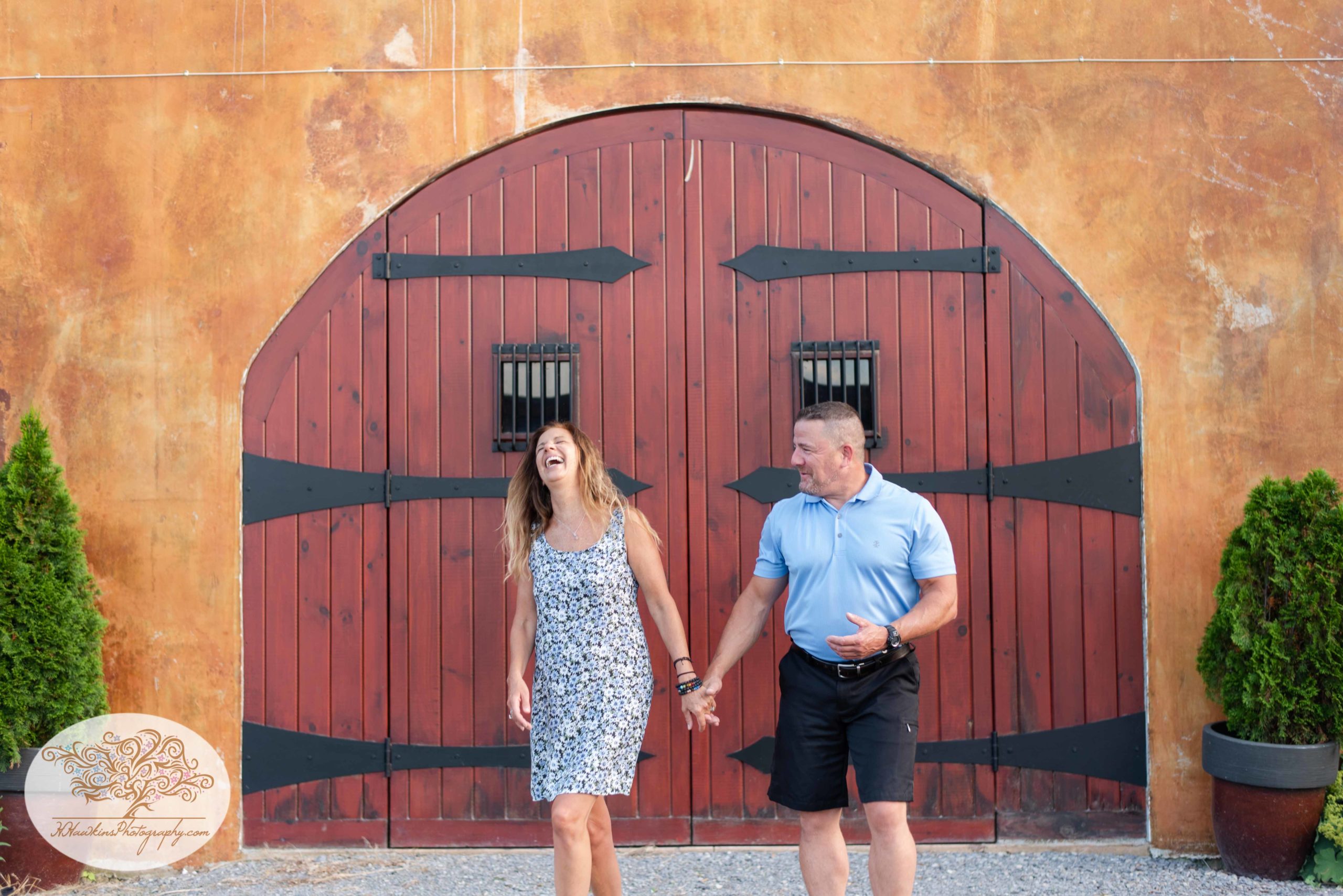 Bride and groom to be walk together in front of red Tuscan looking doors at Anyela's Vineyard in Skaneateles NY