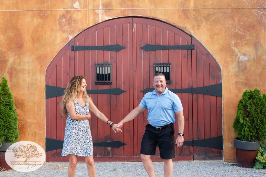 Bride and groom to be walk together in front of red Tuscan looking doors at Anyela's Vineyard in Skaneateles NY