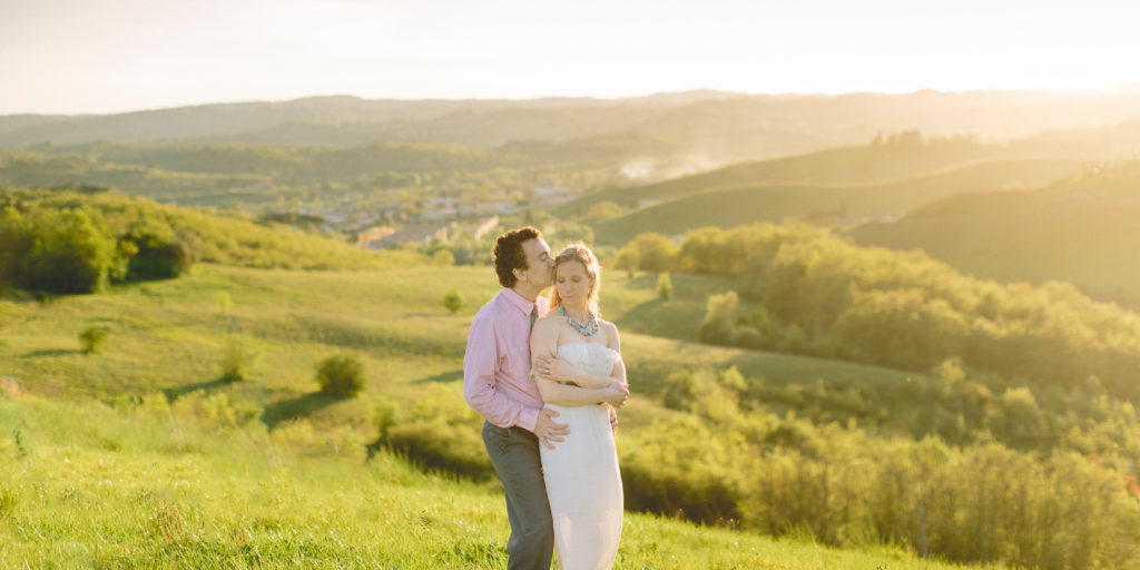 couple stand in field in Tuscany Italy with man kissing girl's forehead
